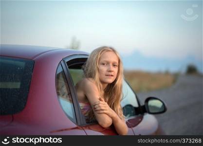 autotravel with children. happy smiling little girl looking out the car window and sunset at the background