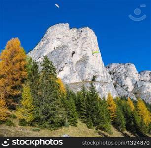 Autumn alpine Dolomites mountain scene and unrecognizable paragliders in sky. Peaceful view near Wolkenstein in Groden, Selva di Val Gardena, Sudtirol, Italy. Picturesque traveling, seasonal, nature and countryside beauty concept scene.