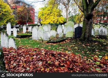 Autumn ancient graveyard with orange leaves and green grass in England. Spooky old cemetery for Halloween themes and decoration.