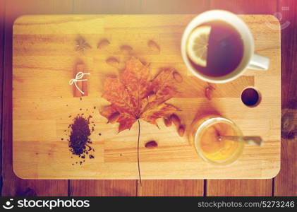 autumn and ethnoscience concept - cup of lemon tea and honey on wooden board with maple leaf and almond. cup of lemon tea and honey on wooden board