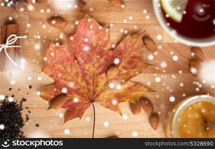 autumn and ethnoscience concept - cup of lemon tea and honey on wooden board with maple leaf and almond over snow. cup of lemon tea and honey on wooden board