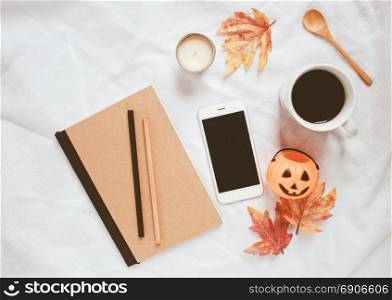 Autumn and halloween style concept, notebook and smartphone with coffee on white bed sheet background