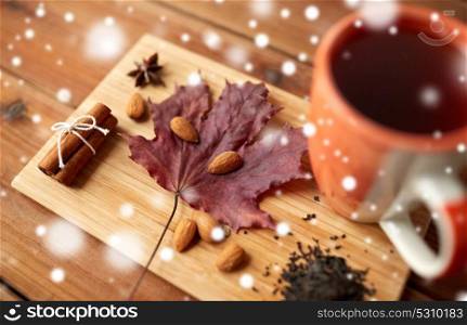 autumn and season concept - cup of tea, maple leaf and almond on wooden board over snow. cup of tea, maple leaf and almond on wooden board