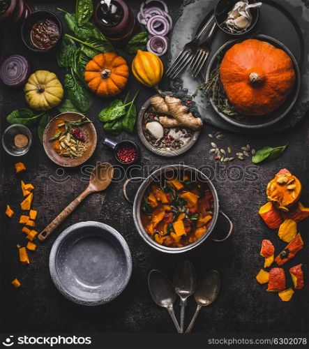 Autumn and winter cooking and eating with pumpkin dishes. Vegetarian stew in cooking pot with spoon and vegetables ingredients on dark kitchen table background, top view. Healthy seasonal food