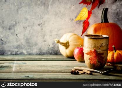 Autumn background with cup of tea or coffee, pumpkins, pumpkin pie spices and leaves on wooden tabel against old rust condition vintage wall, space for text