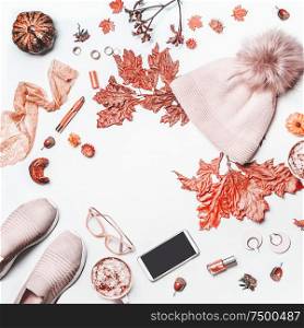 Autumn beauty feminine arrangement on white background with knit hat with pom pom,pumpkin. sneakers, smartphone with mock up , fall leaves, cosmetics and mug with hot chocolate. Top view. Flat lay.