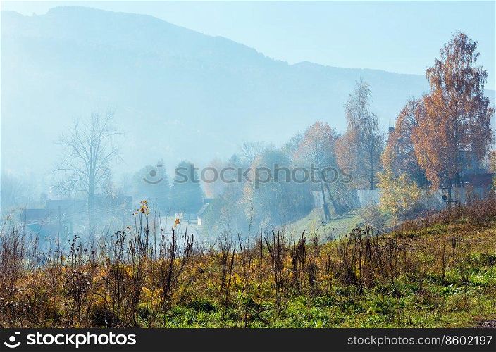 Autumn Carpathian Mountains landscape with multicolored trees and small hamlet on slope, and misty cloud over  Rakhiv district, Transcarpathia, Ukraine .