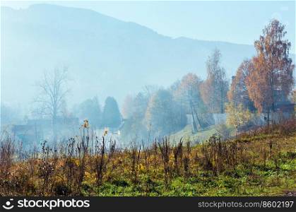 Autumn Carpathian Mountains landscape with multicolored trees and small hamlet on slope, and misty cloud over  Rakhiv district, Transcarpathia, Ukraine .