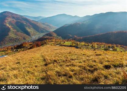 Autumn Carpathian Mountains landscape with multicolored yellow-orange-red-brown trees on slope and  Rakhiv town and Tysa river in far below  view from Rakhiv pass, Transcarpathia, Ukraine .