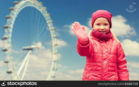 autumn, childhood, gesture, nature and people concept - happy little girl waving hand over london ferry wheel and blue sky background