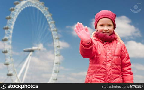 autumn, childhood, gesture, nature and people concept - happy little girl waving hand over london ferry wheel and blue sky background