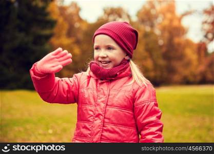autumn, childhood, gesture, nature and people concept - happy little girl waving hand in park. happy little girl waving hand in autumn park