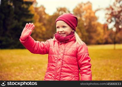 autumn, childhood, gesture, nature and people concept - happy little girl waving hand in park