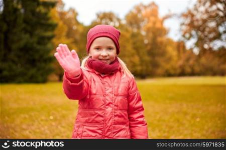 autumn, childhood, gesture, nature and people concept - happy little girl waving hand in park