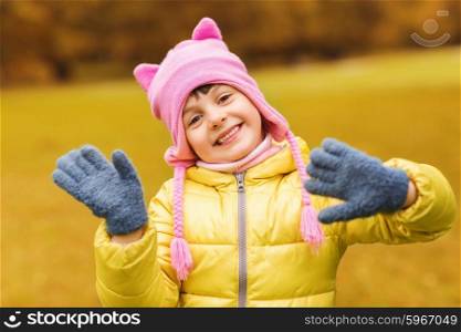 autumn, childhood, happiness and people concept - happy beautiful little girl waving hands outdoors