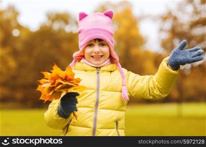 autumn, childhood, happiness and people concept - happy beautiful little girl with maple leaves bunch waving hand outdoors