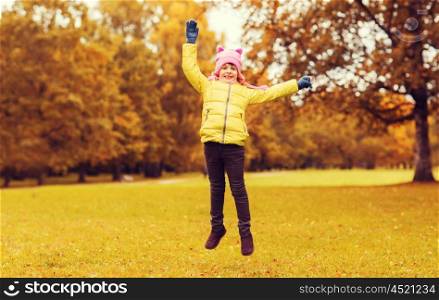 autumn, childhood, happiness and people concept - happy little girl with raised hands jumping and having fun outdoors