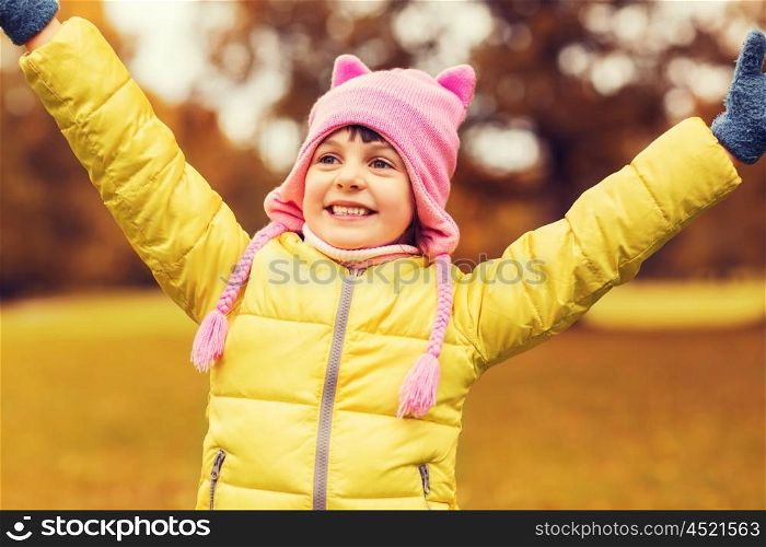 autumn, childhood, happiness and people concept - happy little girl with raised hands having fun outdoors
