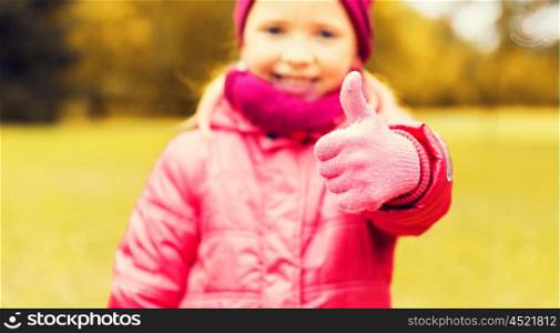 autumn, childhood, happiness, gesture and people concept - close up of happy little girl showing thumbs up outdoors