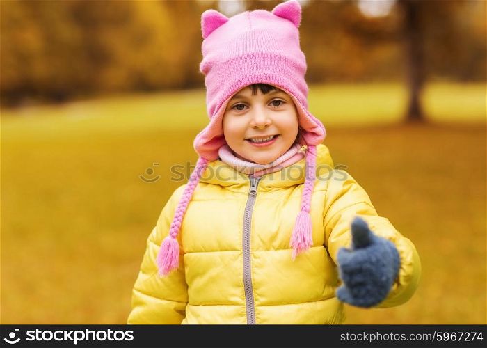 autumn, childhood, happiness, gesture and people concept - happy beautiful little girl showing thumbs up outdoors