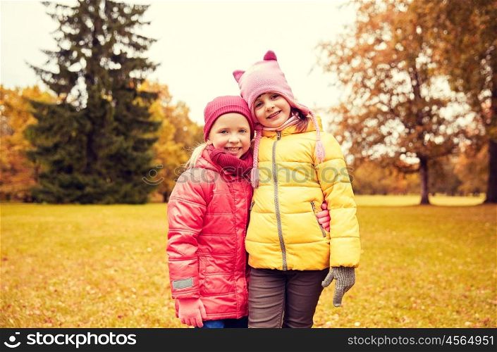 autumn, childhood, leisure and people concept - two happy little girls hugging in park