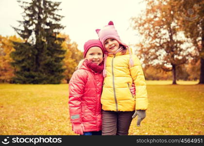 autumn, childhood, leisure and people concept - two happy little girls hugging in park