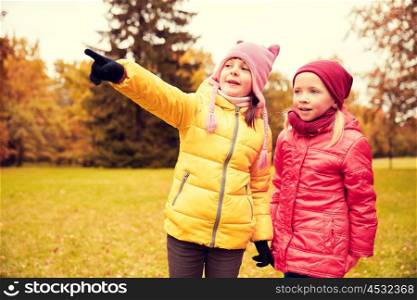 autumn, childhood, leisure, gesture and people concept - happy little girls pointing finger in park outdoors