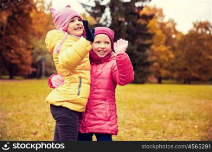 autumn, childhood, leisure, gesture and people concept - happy little girls waving hands in park outdoors