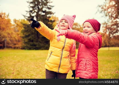 autumn, childhood, leisure, gesture and people concept - two happy little girls pointing finger to something in autumn park