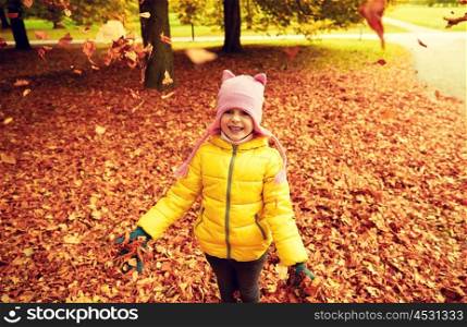autumn, childhood, nature and people concept - happy little girl playing with fallen leaves in park