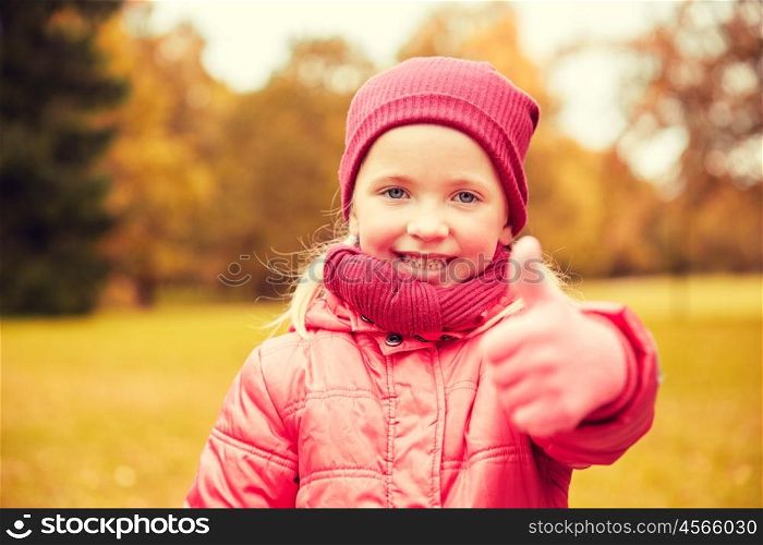 autumn, childhood, nature and people concept - happy little girl showing thumbs up in park