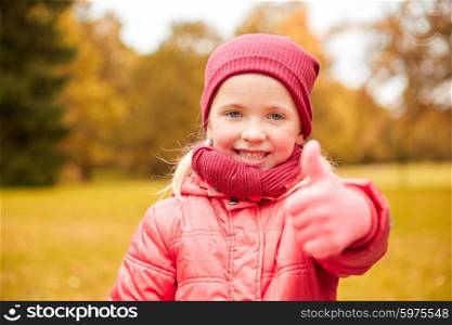 autumn, childhood, nature and people concept - happy little girl showing thumbs up in park