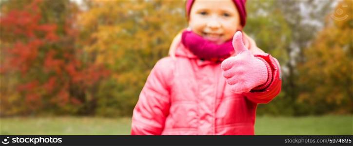 autumn, childhood, season, gesture and people concept - close up of happy little girl showing thumbs up outdoors over natural background