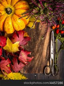 Autumn composing with foliage, pumpkin and vintage scissors on rustic wooden background, top view