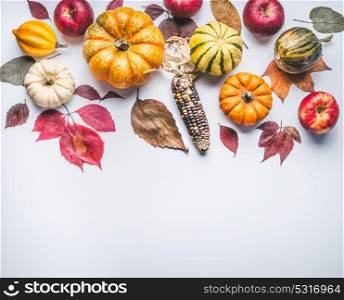 Autumn composing with pumpkin,corn , apples and leaves on light background, top view. Fall border made of natural organic farm products.