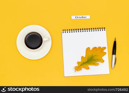 Autumn composition. Text October Coffee Cup, empty open notepad with pen and yellow oak leaf on yellow paper background. Top view Flat lay Mockup. Text October Coffee Cup, empty open notepad with pen and yellow oak leaf on yellow background.