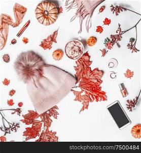 Autumn concept with knit hat with pom pom, woolen scarf, pumpkin. smartphone , fall leaves , cosmetics and mug with hot chocolate. Top view. Flat lay. Blog feminine arrangement on white background