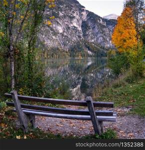 Autumn evening alpine view. Bench near peaceful mountain lake with clear transparent water and reflections. Almsee lake, Upper Austria.