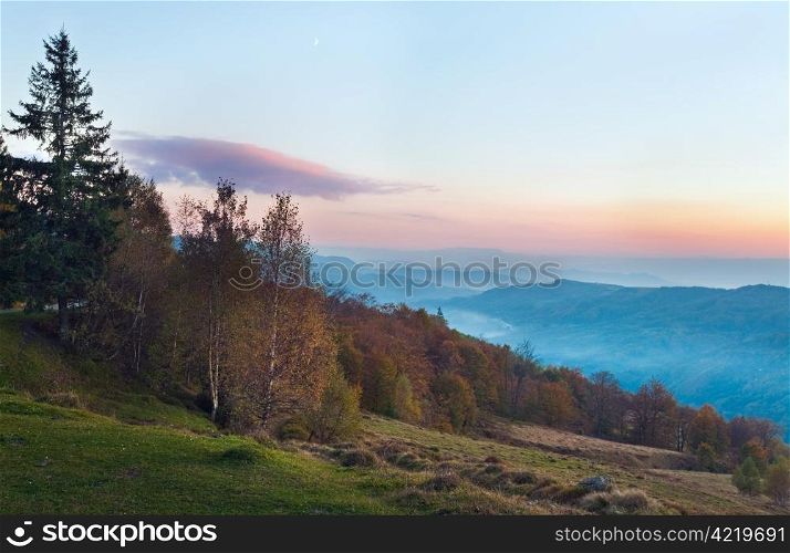 Autumn evening landscape with lust sunlight on mountains and pink glow in sky