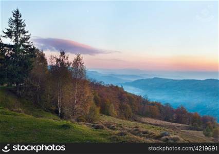 Autumn evening landscape with lust sunlight on mountains and pink glow in sky