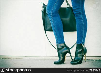 Autumn fashion outfit. Fashionable woman long legs in denim pants black stylish high heels shoes and handbag outdoor on city street