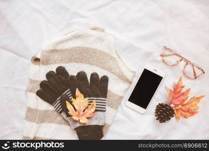 Autumn fashion style concept, sweater and smartphone with maple leaves on white bed sheet background