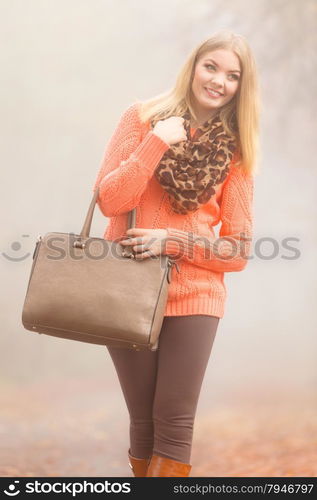 Autumn fashion. Woman fashionable girl wearing vivid clothing holding brown leather bag handbag in hand, walking in autumnal foggy park, outdoors