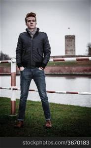 Autumn fashion. Young handsome man male model in full length casual style hair styling posing outdoor, cold autumnal foggy day, historical tower in the background