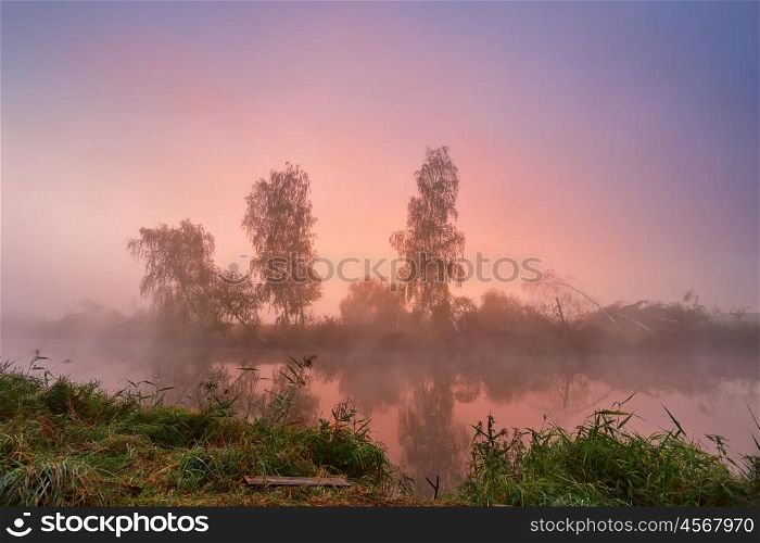 Autumn foggy morning. Colorful dawn on the misty calm river