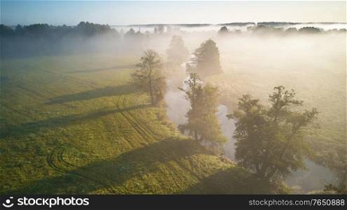 Autumn foggy sunrise aerial view. Colorful misty morning dawn. Fall rural scene. Small river with trees in meadow and field, Belarus
