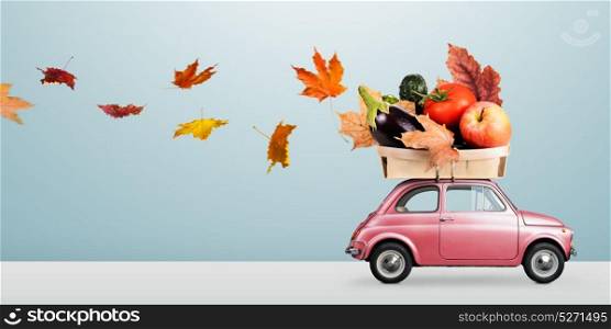 Autumn food delivery. Food delivery. Autumn red toy car with fallen leaves delivering fruits and vegetables against business district buildings