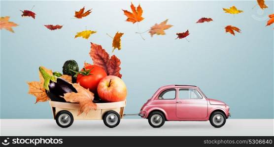 Autumn food delivery. Food delivery. Autumn red toy car with fallen leaves delivering fruits and vegetables against business district buildings