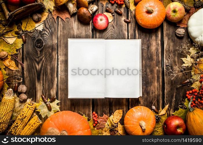 Autumn food. Old book with autumn fruits and vegetables. On wooden background.. Old book with autumn fruits and vegetables.
