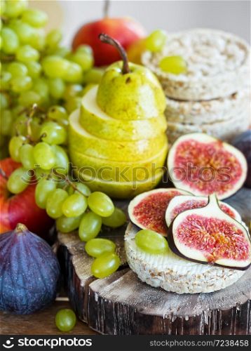 Autumn, fresh fruits. In the foreground are sliced figs and a pear located on a wooden tray. Close-up.